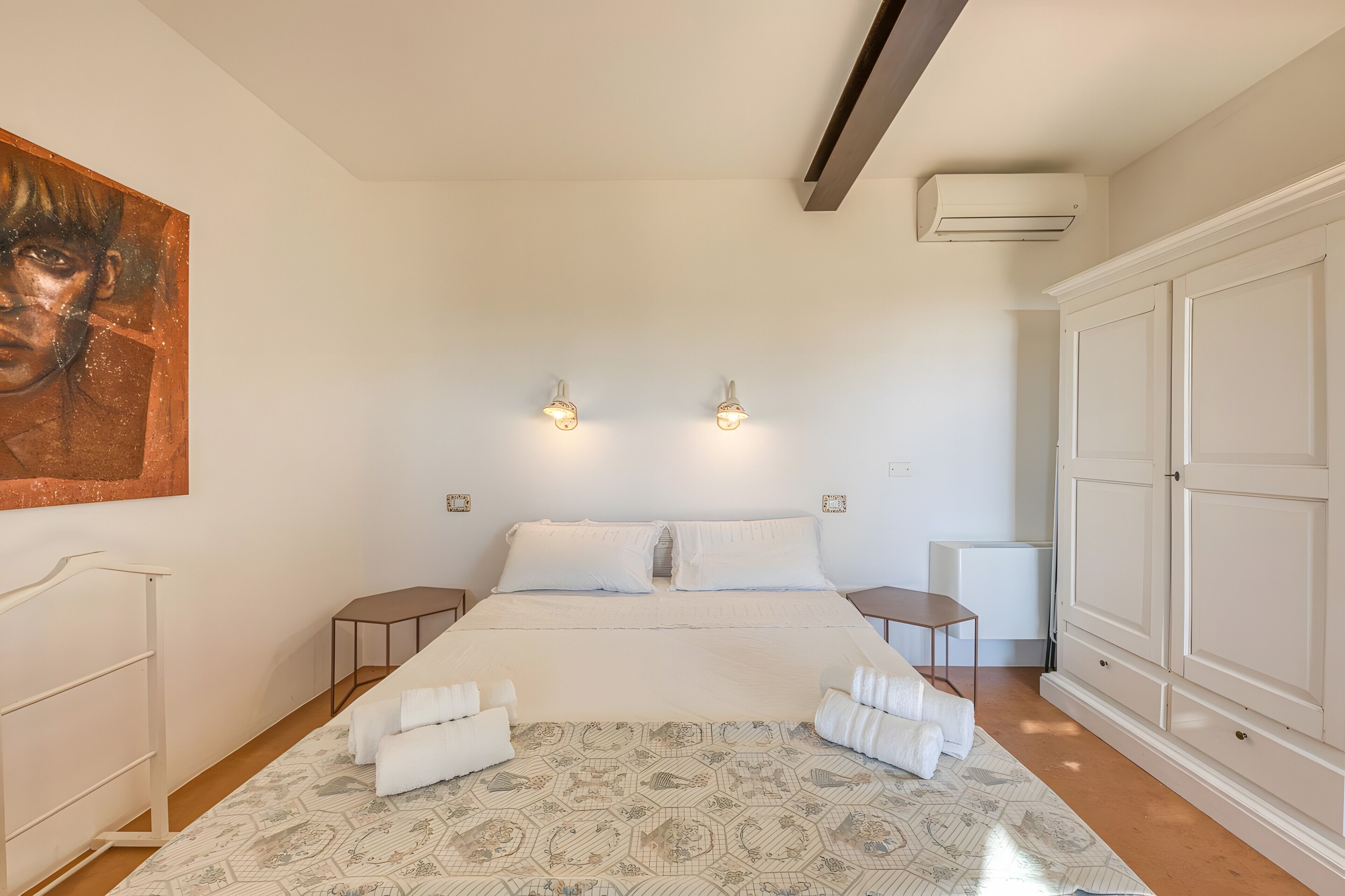 A bedroom with a bed, bedside tables, a wardrobe, and a painting on the wall.