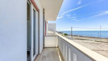 Een balkon met uitzicht op zee, een hekwerk en een deur die leidt naar de binnenruimte.
