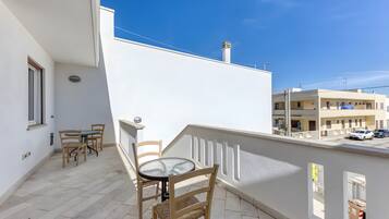 Een balkon met een tafel en stoelen, een wit gebouw en een helderblauwe lucht.