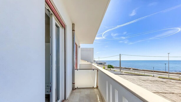 A balcony with a view of the sea, a clear sky, and a distant shoreline.