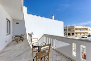 Un balcon avec une table et des chaises, un bâtiment blanc et un ciel bleu dégagé.