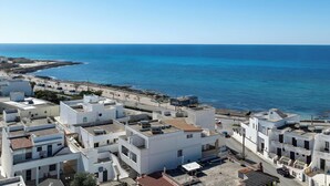 A coastal town with white buildings, a clear blue sea, and a paved promenade.