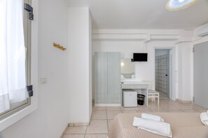 Habitación de hotel con cama, escritorio, refrigerador pequeño, televisor y baño con ducha.