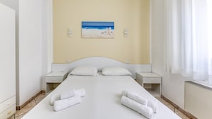 A hotel room with a bed, two bedside tables, a painting of a beach scene, and a window with curtains.