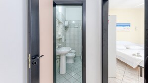 A bathroom with a sink, toilet, and bidet; a bed with white linens; and a painting on the wall.