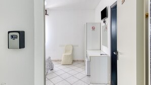 A narrow hallway with a white door, a white wall-mounted television, a white refrigerator, and a white chair. - Inn 'Doppia 3' with Balcony, Wi-Fi and Air Conditioning (Torre San Giovanni Ugento)