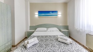A bedroom with a bed, nightstands, a headboard, a painting, and towels. - Inn 'Doppia 4' with Wi-Fi and Air Conditioning (Torre San Giovanni Ugento)