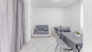 A room with a grey sofa, a dining table with chairs, and a potted cactus. - Inn 'Doppia 4' with Wi-Fi and Air Conditioning (Torre San Giovanni Ugento)