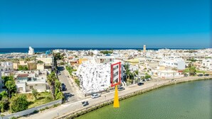 A coastal cityscape with a prominent white building with a red and white sign, a clear blue sky, and a calm sea. - Inn 'Quadrupla 1' with Wi-Fi and Air Conditioning (Torre San Giovanni Ugento)