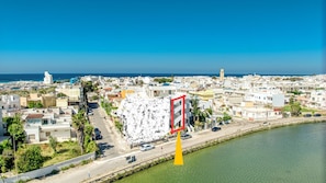 A coastal cityscape with a prominent white building with a red and white sign, a clear blue sky, and a calm sea.