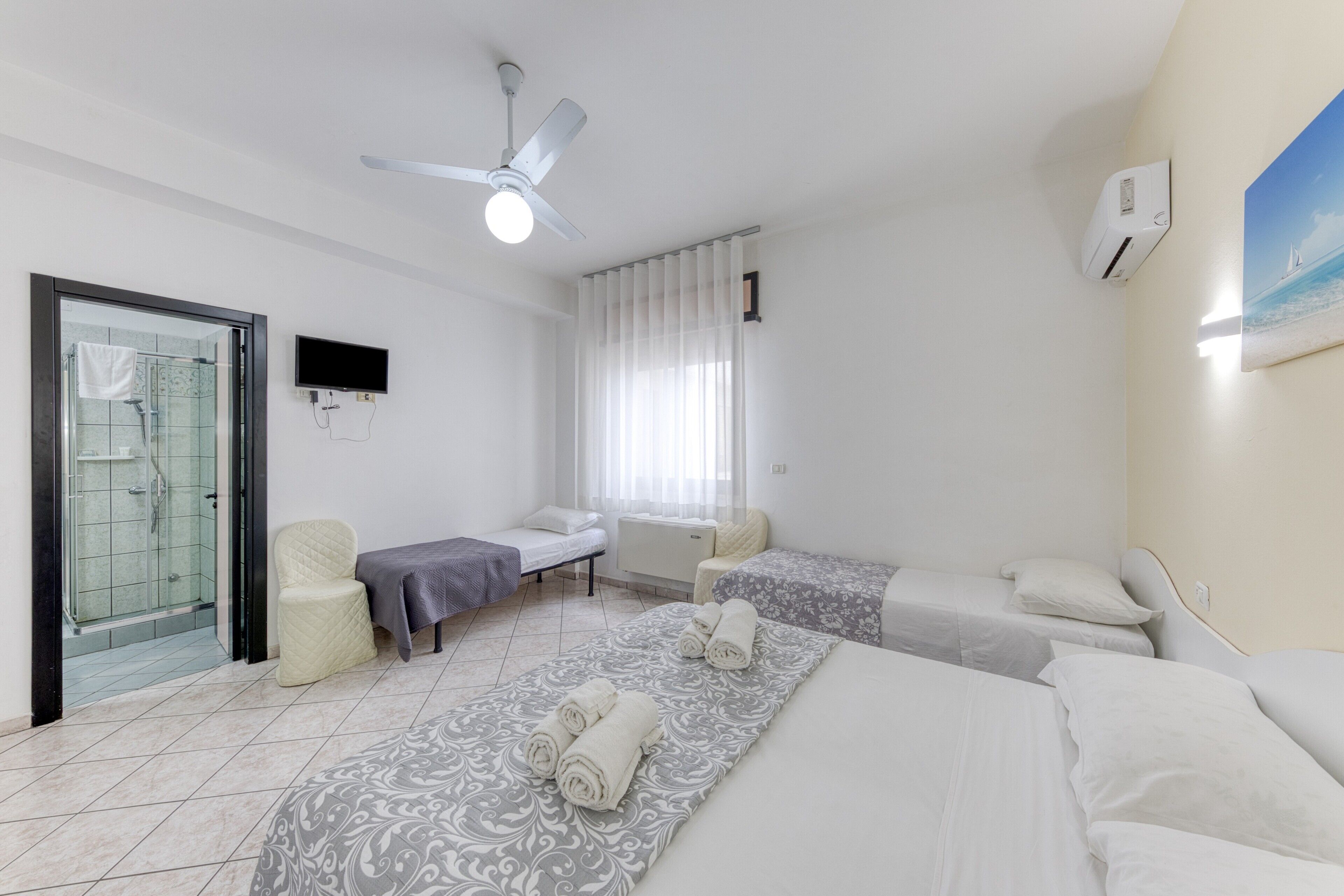 Ein Hotelzimmer mit zwei Betten, einer Dusche, einem Deckenventilator, einem Fernseher und einem Bild an der Wand.
