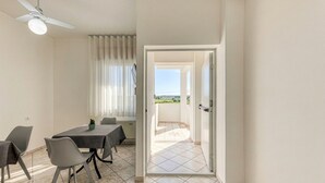 A dining area with a table and chairs, a ceiling fan, and a view through an open door to a balcony with a tiled floor. - Inn 'Quadrupla 2' with Wi-Fi and Air Conditioning (Torre San Giovanni Ugento)