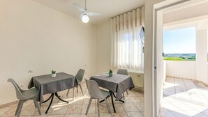 Un espace repas comprenant deux tables, des chaises, un ventilateur de plafond et une vue par une fenêtre.