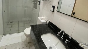 Et moderne badeværelse med et glasafskærmet brusebad, et hvidt toilet, en vask i sort marmor og et stort spejl.