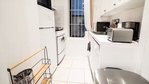 Una cucina compatta con elettrodomestici bianchi, una finestra con inferriate e vista sull'esterno.