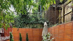 Un'area patio con mobili in vimini, prato artificiale verde e recinzione in legno.