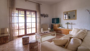 A living room with a sofa, a coffee table, a television, and a dining area with chairs and a table. - Villa Aetos (Rethymno)