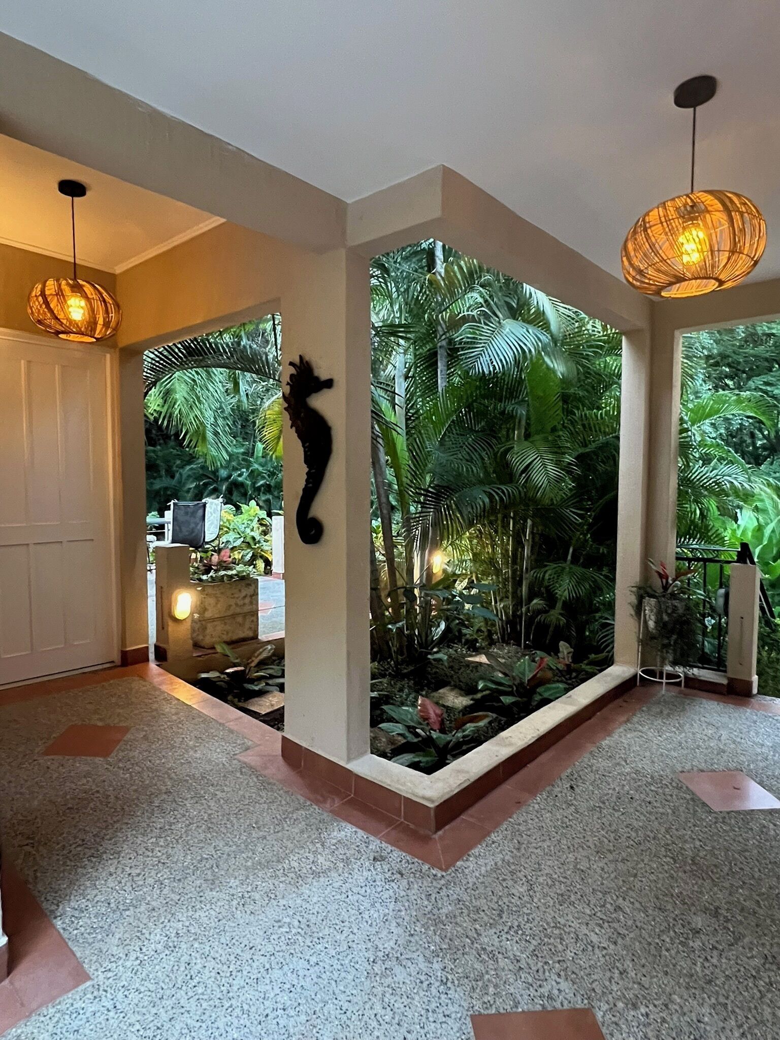 Un hall d’entrée spacieux donnant sur un jardin tropical, agrémenté d’une décoration murale représentant des hippocampes et d’un luminaire suspendu.