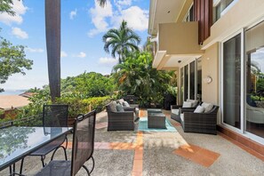 A balcony with wicker furniture, a glass table, and a view of the beach.
