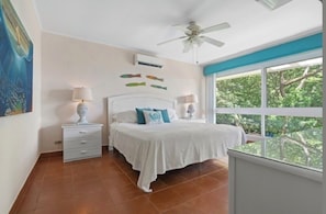 A bedroom with a bed, nightstands, a ceiling fan, and a window with a view of trees.