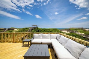A wooden deck with a sofa and table, a gazebo, and a view of the beach. - Nags Head Oceanfront w/ Pool, Sauna, Hot Tub! (Nags Head)
