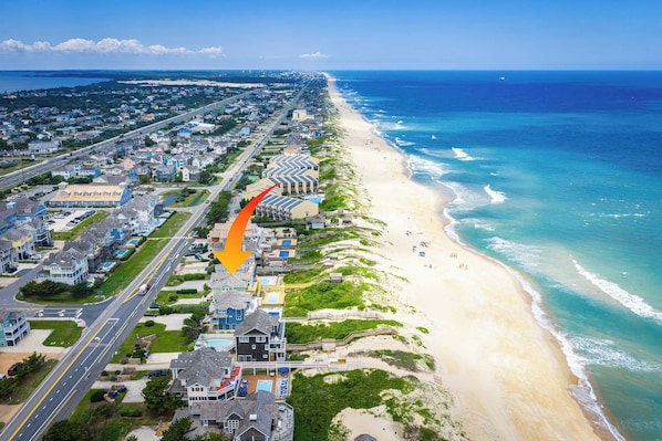 Vista aérea de un pueblo costero con una playa, una carretera que recorre la costa en paralelo, y una combinación de edificios residenciales y comerciales.