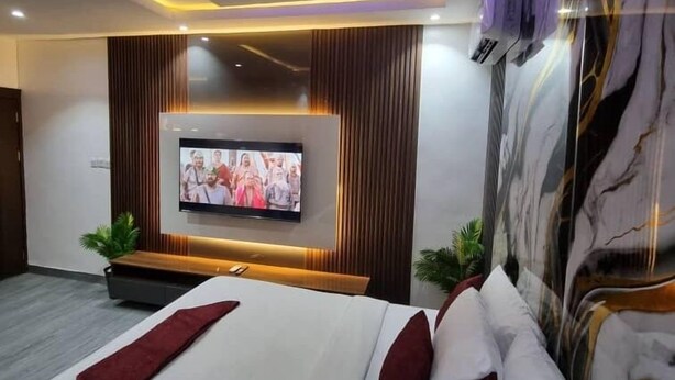 A modern hotel room with a large bed, a flat-screen TV mounted on the wall, and a marble accent wall. - Hotel Guidotti (Abuja)