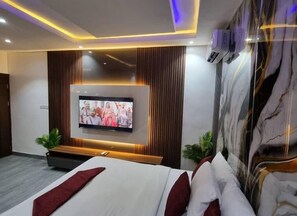 A modern hotel room with a large bed, a flat-screen TV mounted on the wall, and a marble accent wall. - Hotel Guidotti (Abuja)