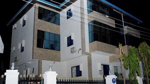 A modern two-story building with a gated entrance, large windows, and a visible blue sign on the gate. - Hotel Guidotti (Abuja)