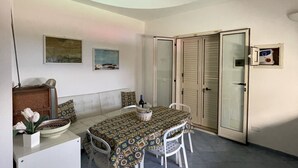 A dining area with a table set for two, a sofa, and a cabinet with a vase of flowers. - Villa Alice is an independent newly built villa, designed in the traditional “dammuso” style with its characteristic dome and overlooking the sea. It is a retreat immersed in nature, perfect for those seeking peace, privacy and an authentic stay. The (Marina di Caronia)