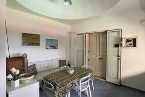 Ein Essbereich mit einem Tisch für zwei Personen, einer Couch und einem Schrank mit einer Blumenvase.