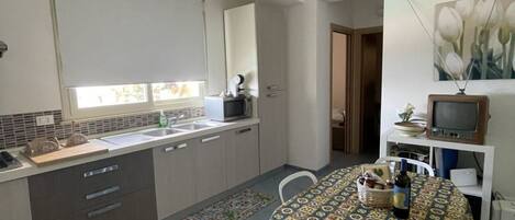 A compact kitchen with a dining area, a microwave, a sink, and a television.