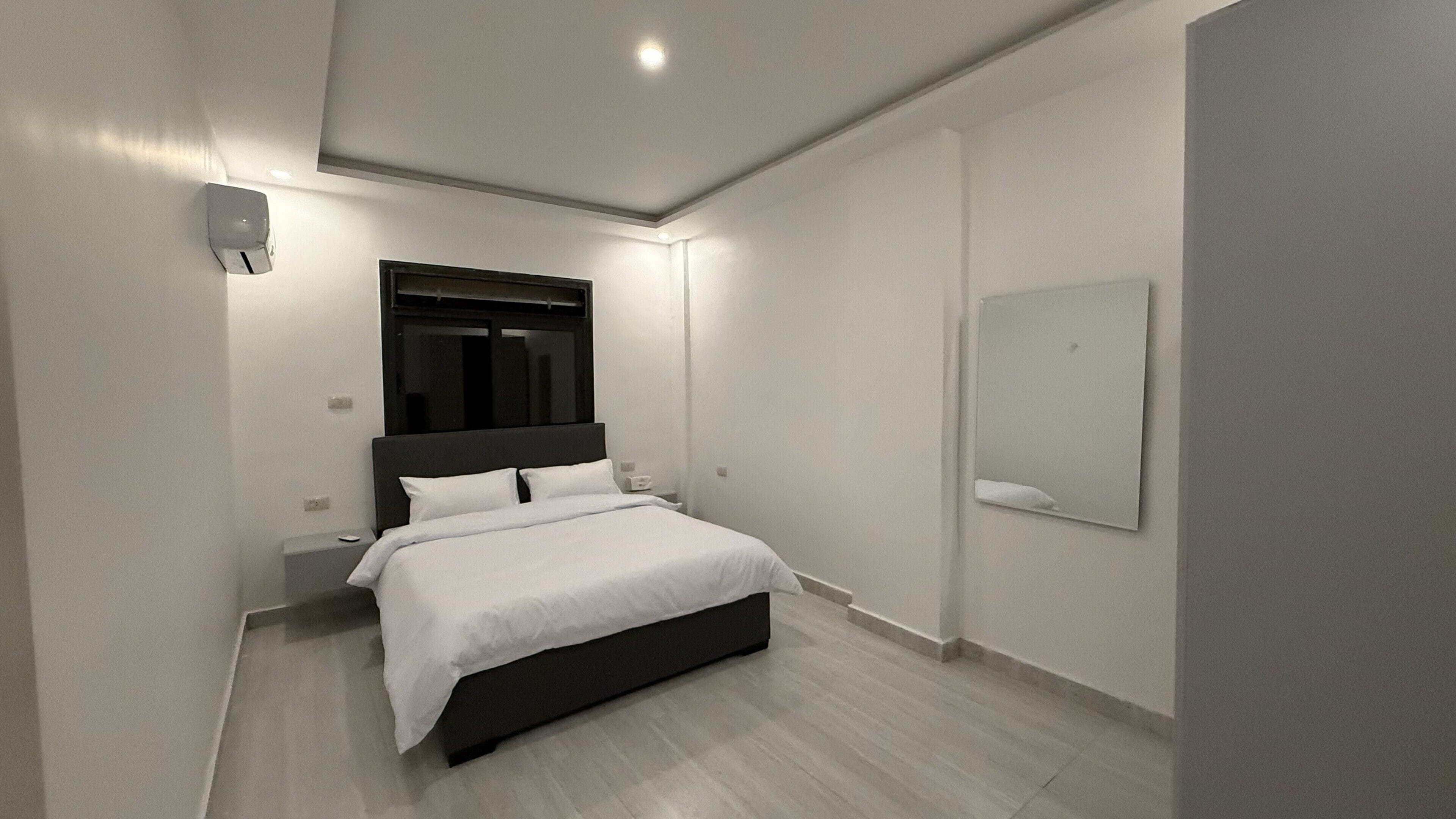 A modern bedroom with a bed, bedside tables, a mirror, and a ceiling light.