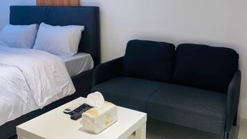 Ett modernt hotellrum med en säng, en mörk soffa och ett litet vitt bord med en fjärrkontroll och en ask med pappersnäsdukar.