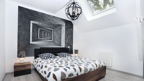 Un dormitorio moderno con una cama grande, una mesita de noche, una lámpara de pared y un tragaluz.
