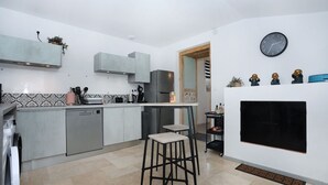Una cocina moderna con gabinetes grises, lavavajillas integrado, una isla central y un televisor con marco negro en la pared.