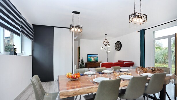 Un comedor moderno con una mesa de madera, sillas grises y un frutero. Hay dos lámparas colgantes sobre la mesa.