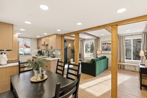 A modern kitchen with wooden cabinets, a dining table with chairs, and a view of a snowy landscape through large windows. - Walk to Ski, 2 Kings, Luxury Park City Condo (Park City)