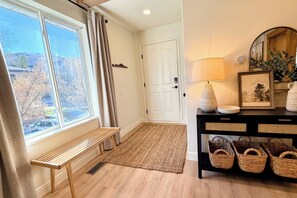 A room with a bench by a window, a door, a lamp, and baskets on a console table. - Walk to Ski, 2 Kings, Luxury Park City Condo (Park City)