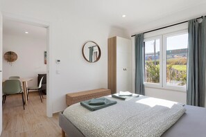 A bedroom with a bed, a bedside table, a mirror, a window with curtains, a desk with chairs, and a view of the outdoors. - Apartment '2' with Shared Pool, Private Terrace and Wi-Fi (Lourinhã)