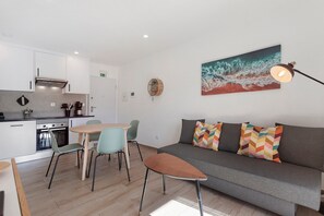 A modern kitchen with white cabinets, a dining table with chairs, a sofa with colorful cushions, and a painting on the wall. - Apartment '2' with Shared Pool, Private Terrace and Wi-Fi (Lourinhã)