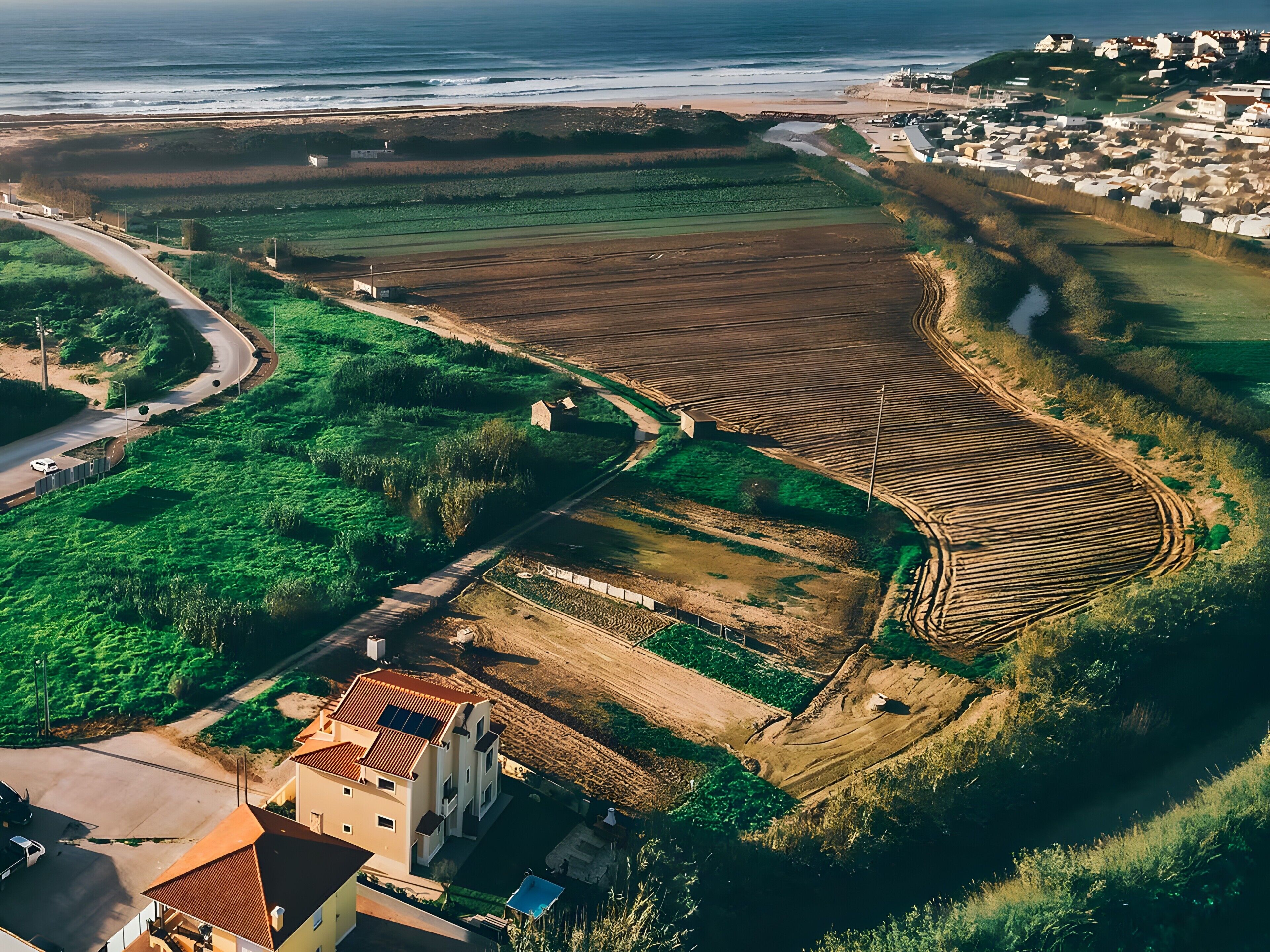 An aerial view of a coastal area with fields, a road, and residential buildings.