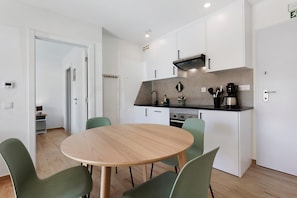 A modern kitchen with white cabinets, a round wooden table, and green chairs. - Apartment '2' with Shared Pool, Private Terrace and Wi-Fi (Lourinhã)