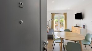 Una habitación moderna con una puerta que indica '2', una mesa de comedor con sillas, un televisor montado en la pared y una ventana con cortinas.