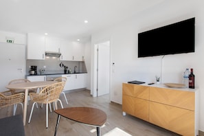 A modern kitchen with white cabinets, a dining area with wicker chairs, a wooden dining table, and a flat-screen TV mounted on the wall. - Apartment '6' with Shared Pool, Shared Terrace and Wi-Fi (Lourinhã)