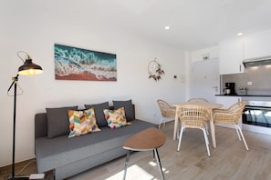 A modern living area with a sofa, a small table, wicker chairs, a painting, a lamp, and a kitchenette. - Apartment '6' with Shared Pool, Shared Terrace and Wi-Fi (Lourinhã)