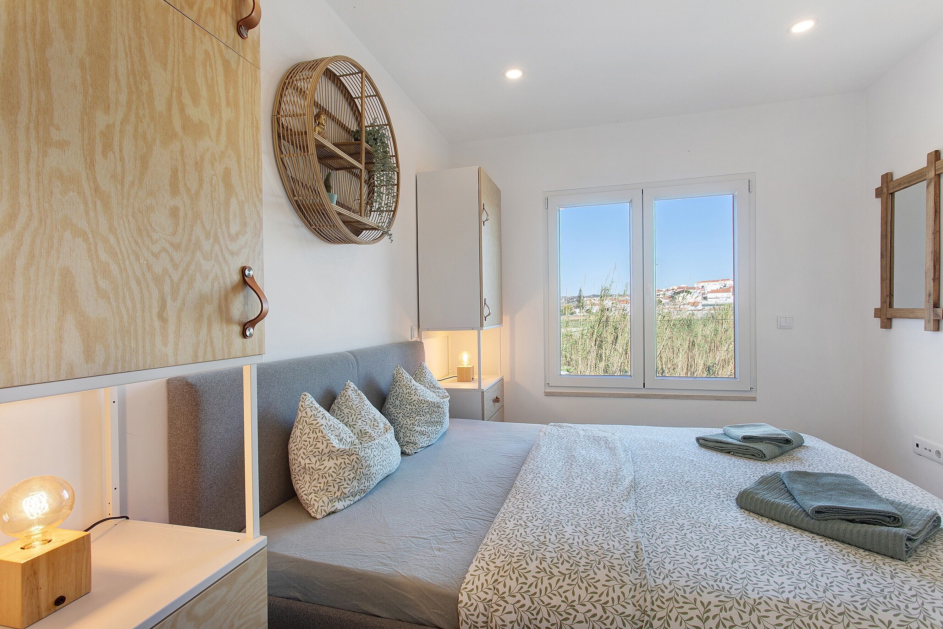 A bedroom with a bed, bedside table, lamp, wall decor, and a window with a view.