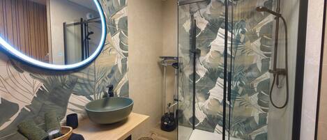 A bathroom with a round mirror, a bowl sink, a shower with glass doors, and a wooden vanity.
