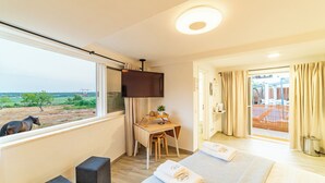 A bedroom with a bed, a desk, a chair, a TV, and a window with a view of the countryside. - Studio with Pool View Terrace (Alcácer do Sal)