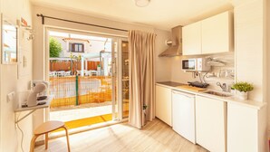 A compact kitchen with a microwave, sink, and a small countertop. A dining area with a chair and a table is visible through an open door. - Studio with Pool View Terrace (Alcácer do Sal)